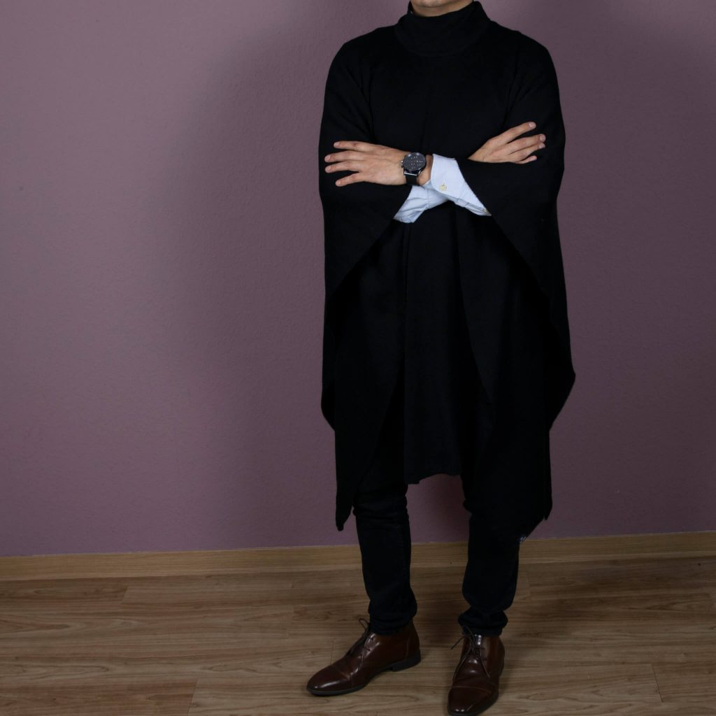 Eleganter Alpaka Poncho für Herren in schwarz von Alpakin, getragen von Mann mit Hemd, der die Arme übereinander legt