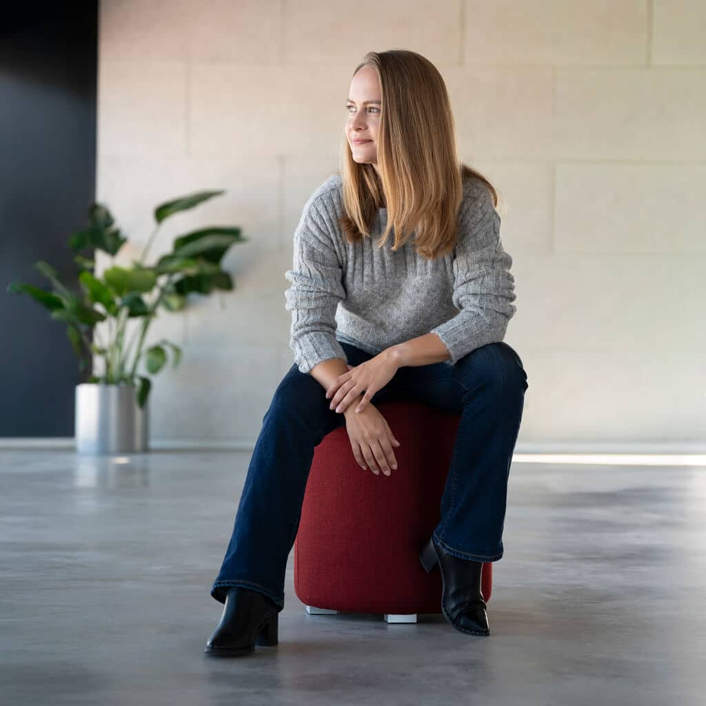 Frau sitzt auf einem roten Hocker und trägt den Andes Alpaka Wollpullover von Alpakin