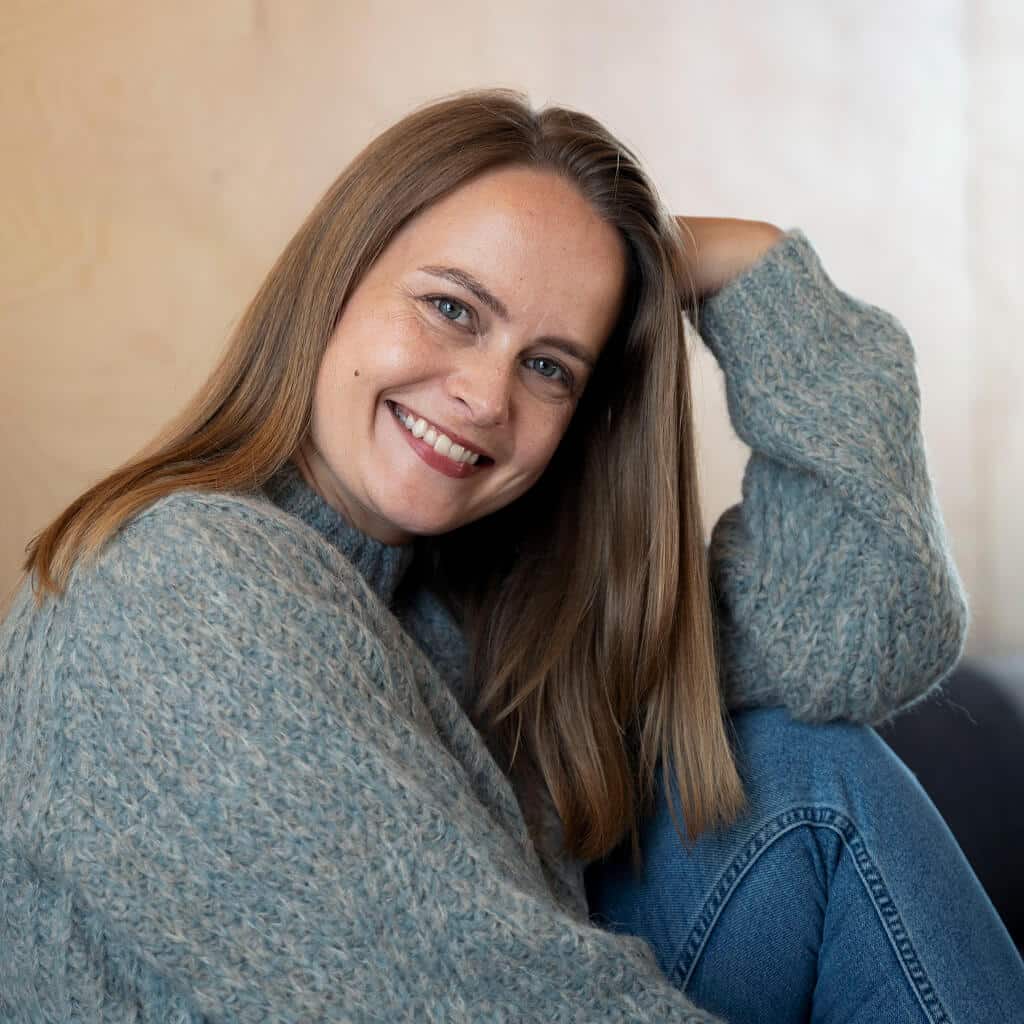 Frau lächelt glücklich in die Kamera. Dank ihres kuschelweichen Alpaka Pullovers fühlt sie sich rundum wohl.