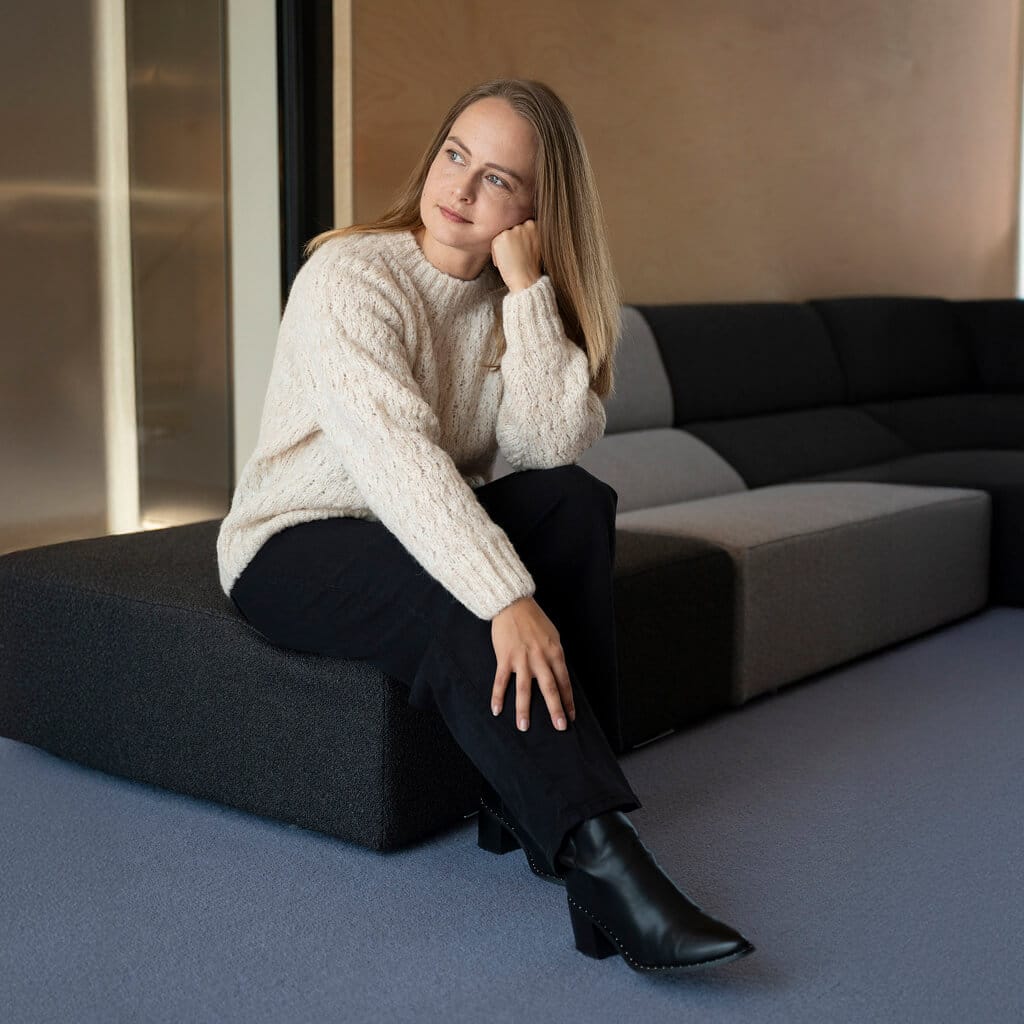 Frau mit Liya Alpaka Pullover in creme mit Zopfmuster sitzt auf einem dunklen Sofa