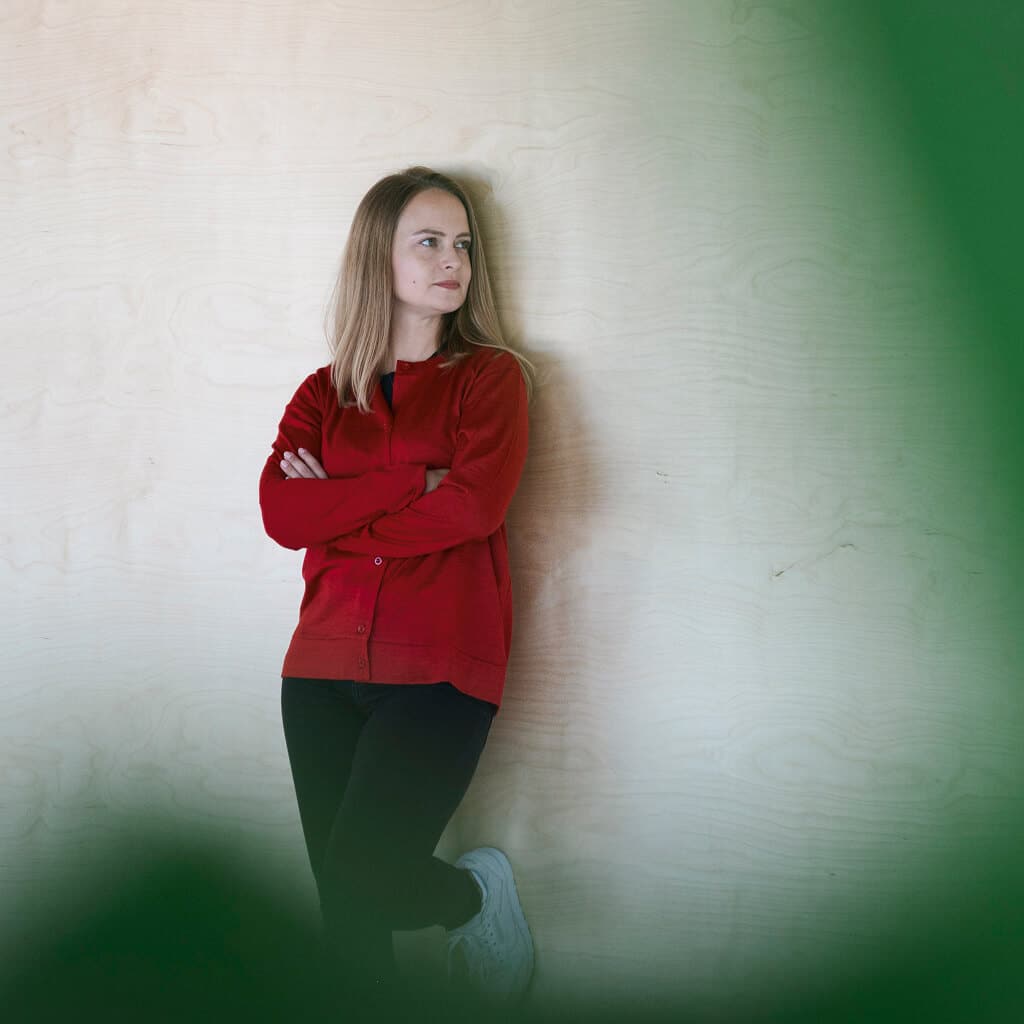Frau lehnt an eine helle Wand und trägt eine Premium Babyalpaka Seide Strickjacke in glänzendem dunkelrot