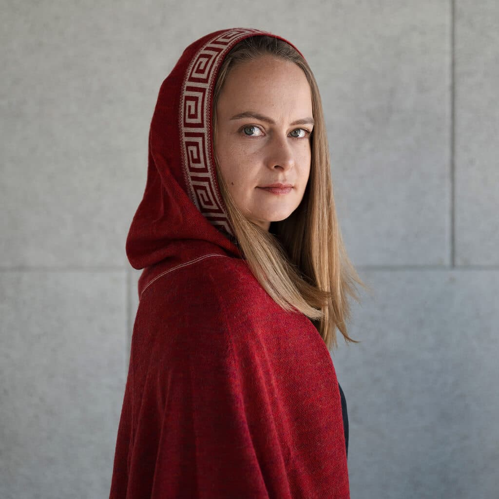 Frau seitlich mit Luz Alpaka Poncho in rot mit Kapuze auf ihrem Kopf