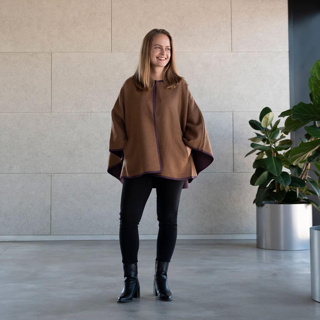 Frau blickt selbstbewusst in die Kamera und trägt den Oro Alpaka Poncho Mantel von Alpakin in gold