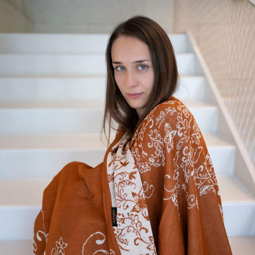 Frau seitlich, trägt ihren Tamaya Alpaka Wendeponcho in dunkelorange mit Blumen Musterung
