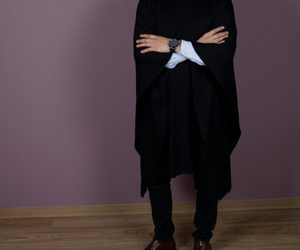 Eleganter Alpaka Poncho für Herren in schwarz von Alpakin, getragen von Mann mit Hemd, der die Arme übereinander legt