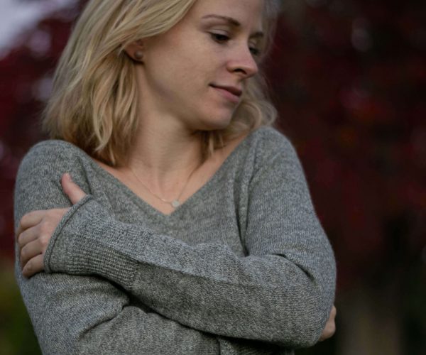 Blonde Frau umarmt sich in ihrem weichen, hellgrauen Alpaka Pullover von Alpakin