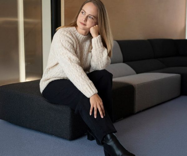 Frau mit Liya Alpaka Pullover in creme mit Zopfmuster sitzt auf einem dunklen Sofa