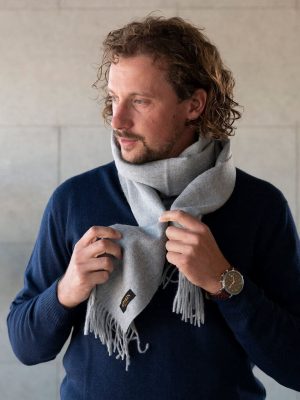 Mann mit Locken trägt einen Naturfarbe Alpaka Schal in hellgrau und einen dunkelblauen Pullover